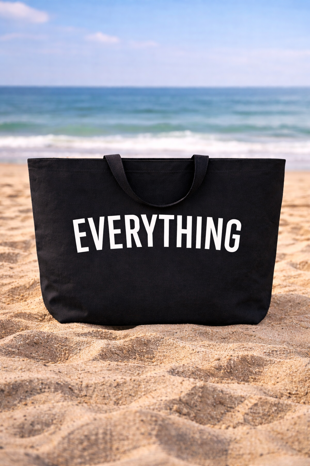 Sac de plage Lucca posé sur le sable avec accessoires de plage autour
